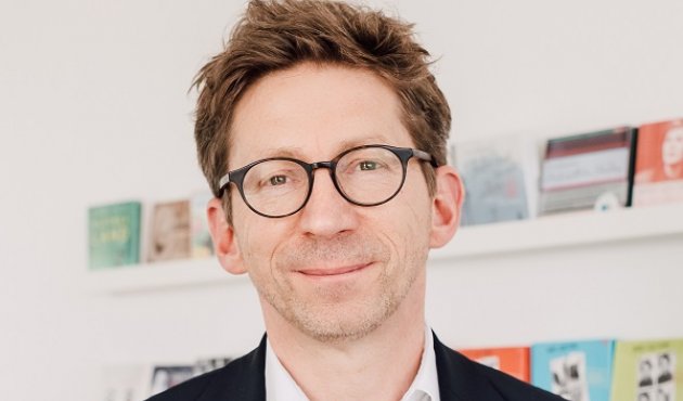 Johannes Stricker im Verlag vor einem Regal mit Hörbüchern 