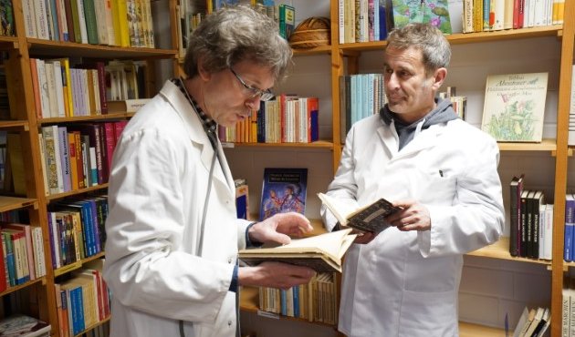Dr. Stefan (Stefan Hauck) und Mr. Ralf (Ralf Schweikart) mit Büchern in Hand und im Ärztekittel umgeben von Büchern