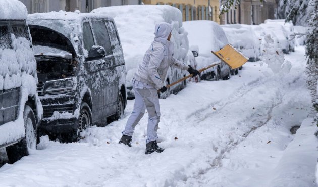 Frau mit Schneeschippe räumt Bürgersteig
