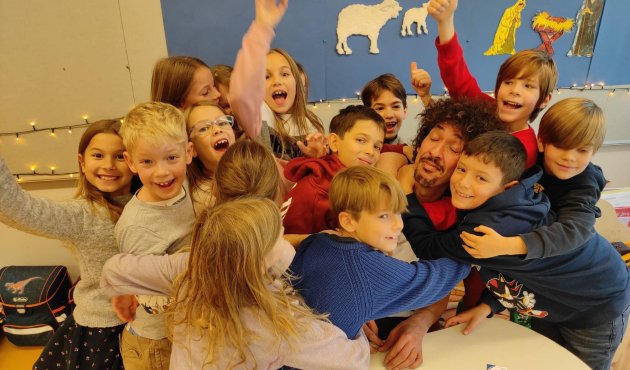 Danny Beuerbach liegt auf dem Boden und wird von einem Dutzend Kinder umarmt