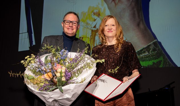 Carsten Brosda und Anja Kampmann mit Blumenstrauß und Preisurkunde auf der Bühne