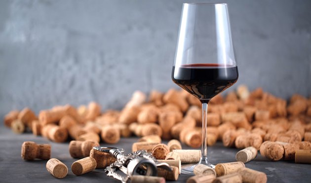 ein mit Rotwein gefülltes Glas steht vor einem Berg Korken
