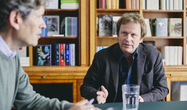 Oliver Vogel im Interview am Schreibtisch, im Vordergrund unscharf der Interviewer Torsten Casimir