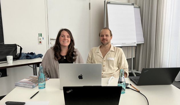 Foto von Laura und Matthias Lackas, am Tisch, hinter ihrem Laptop