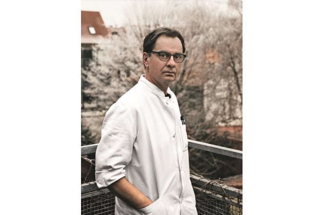Gerhard Steidl auf dem Balkon, blick in die Kamera, er trägt einen weißen Kittel 