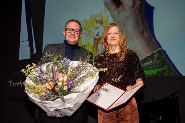 Carsten Brosda und Anja Kampmann mit Blumenstrauß und Preisurkunde auf der Bühne