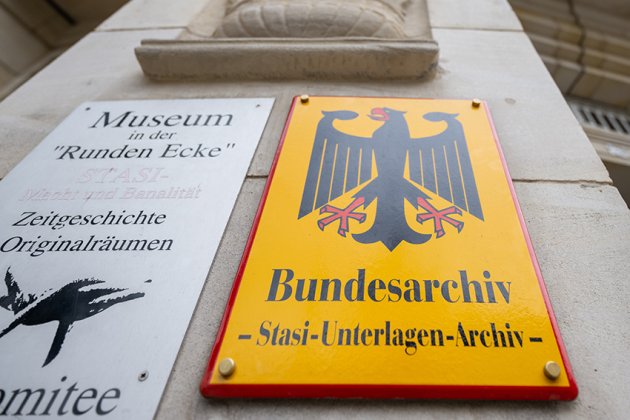 Ein Foto zeigt ein Schild mit der Aufschrift „Bundesarchiv - Stasi-Unterlagen-Archiv“ an der Außenstelle des Bundesarchivs in Leipzig. Das Schild ist gelb mit einem schwarzen Adler und befindet sich neben einem weiteren Schild, das auf ein Museum hinweist. Der Hintergrund zeigt die Fassade des Gebäudes.