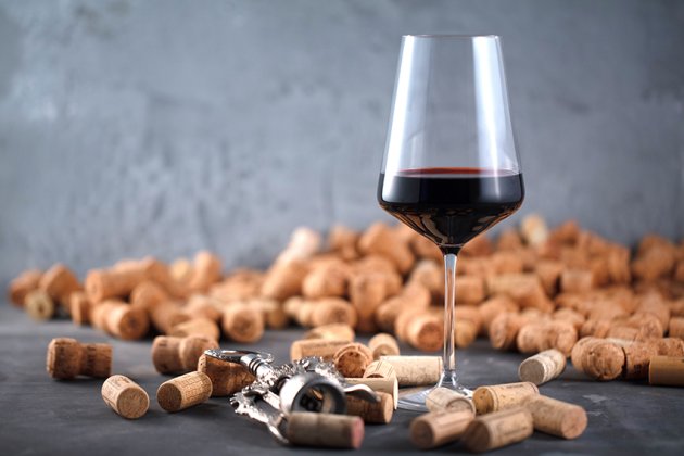 ein mit Rotwein gefülltes Glas steht vor einem Berg Korken