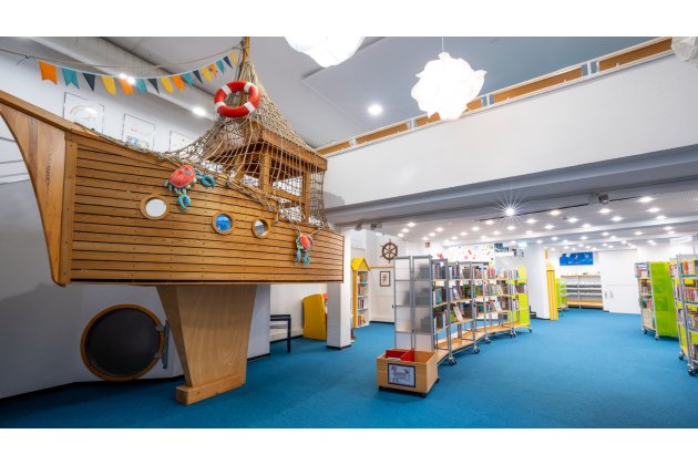 helle, moderne Kinderabteilung in der Bibliothek, mit Bücherregale und einem Schiff zum Hineinklettern 