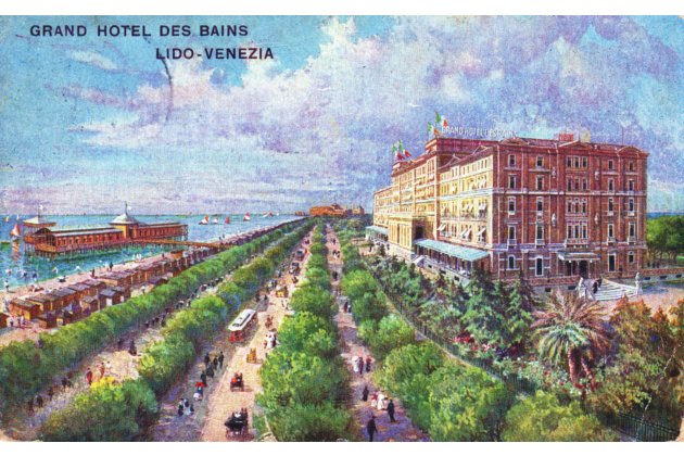 Historische, farbintensive Ansichtskarte vom „Grand Hotel des Bains“ am Lido in Venedig: Rechts steht ein großes, mehrstöckiges Hotelgebäude in warmen Rot- und Ockertönen mit hellen Fensterrahmen und kleinen Flaggen auf dem Dach. In der Bildmitte führt eine breite, von dichtem Grün gesäumte Allee perspektivisch in die Ferne; 