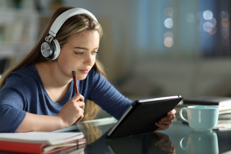 Junge Frau mit Kopfhörern und Tablet beim Lernen