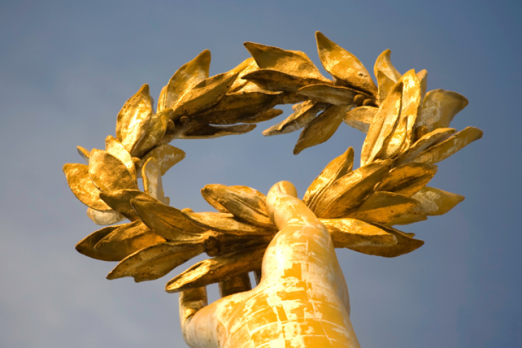 Symbolbild: Eine Hand hält einen goldenen Lorbeerkranz
