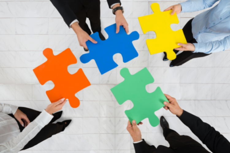 Bunte Puzzleteile werden von Menschen in Business-ANzügen zusammengefügt  