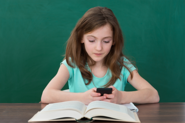 Ein Mädchen mit Handy und aufgeschlagenem Buch vor grünem Hintergrund