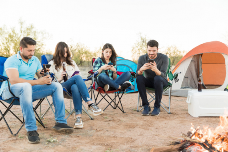 Vier junge Menschen in Campingsesseln - alle haben ein Handy in der Hand