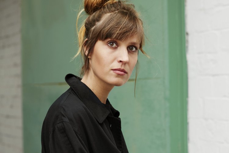 Hochkantaufnahme: Charlotte Gneuß mit zusammengesteckten Haaren und schwarzer Bluse vor grüner Wand