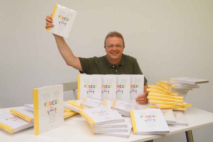 Bernhard Meuser freudestrahlend vor einem YOUCAT-Bücherstapel