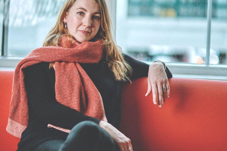 Ailish Jung auf roter Couch vor einer Fensterfront