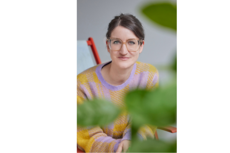 Mona Lang mit Brille hinter einer Pflanze 