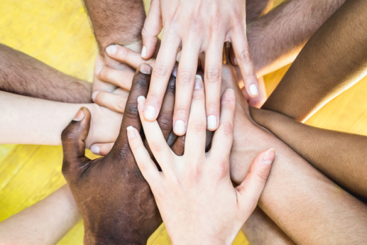 viele Hände in verschiedenen Hauttönen liegen aufeinander