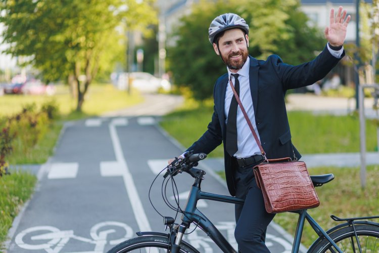 Mann in Bürokleidung, auf einem Fahrrad, winkt zurück