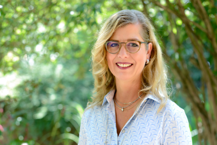 Headshot von Andrea Keller mit Brille vor Bäumen 
