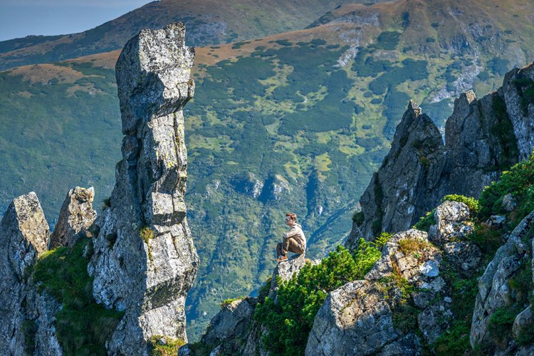 Mann sitzt im Gebirge auf einem Felsvorsprung