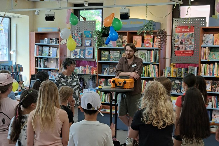 Eine Gruppe Grundschüler hört dem Buchhändler Maximilian Stein in seiner Buchhandlung zu.