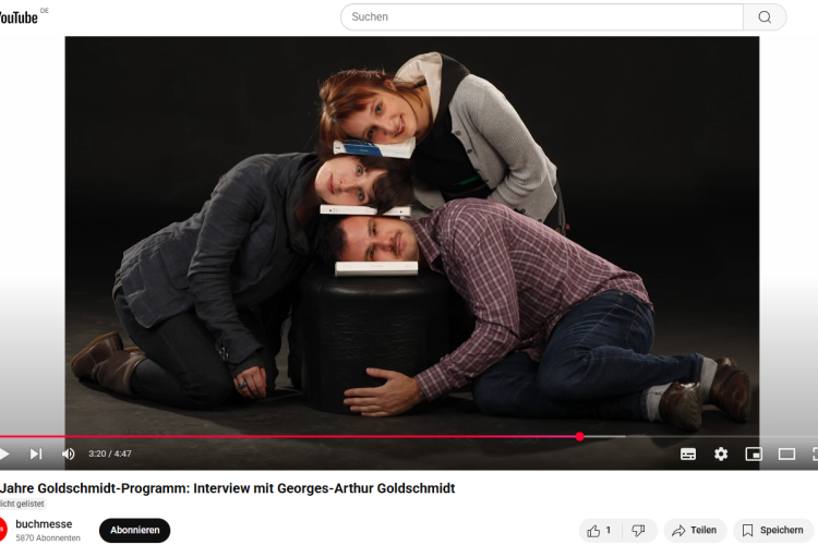 Drei junge Leute knien beieinander, haben ihre Köpfe seitlich übereinandergelegt und Bücher dazwischen gelegt 