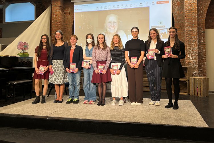Gruppenfoto der Preisträgerinnen (von links nach rechts): Stella Härchen, Sofia Hillebrenner, Lucrezia Wenzler, Charlotte Jelinek, Eliza Dimitrov, Amelie Leufke, Mia Döll, Noémie Meier, Georgina Koberg. Im Hintergrund: Cornelia Funke in der Liveschalte. Megan Haymoz war ebenfalls im Livestream dabei