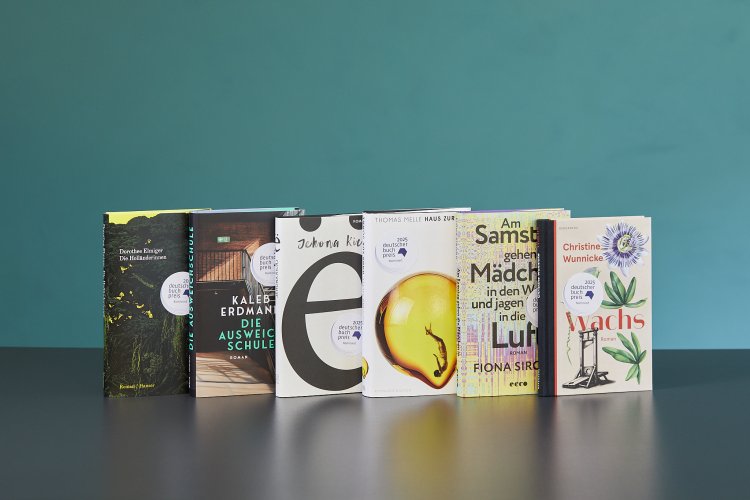 alle 6 für die Shortlist des Deutschen Buchpreises nominierte Bücher stehen nebeneinander auf einem schwarzen Tisch vor grünem Hintergrund