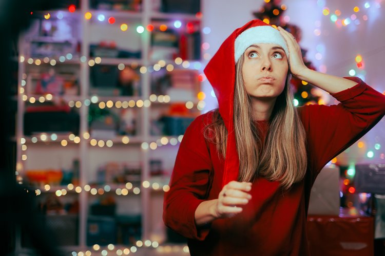 Eine Frau mit Nikolausmütze vor einem Bücherregal bläst die Backen auf und greift sich an die Stirn