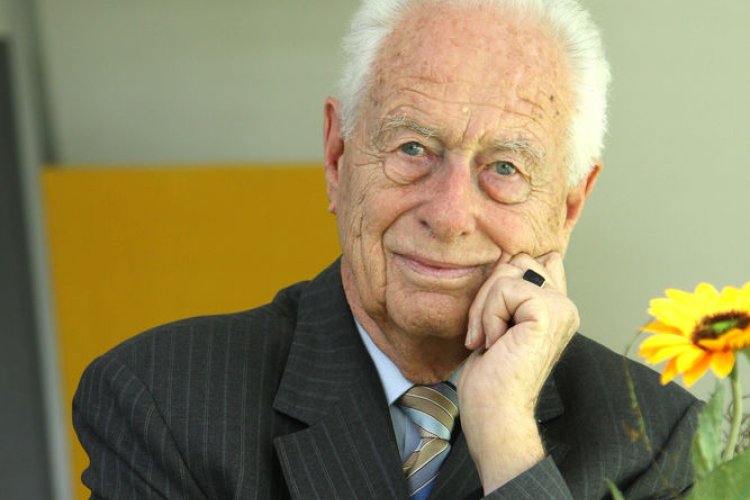 Ernst Tielebier-Langenscheidt sitzt lächelnd an einem Schreibtisch. Im Hintergrund ist das Verlagslogo des Langenscheidt-Verlags zu sehen