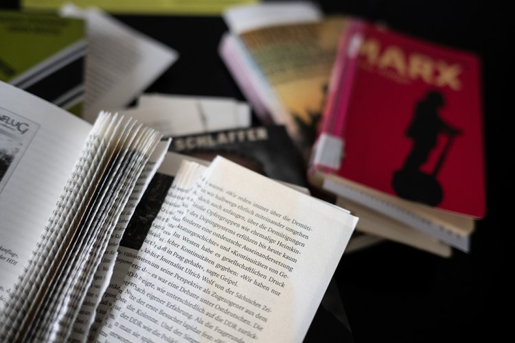 Auf einem Tisch liegen zerstörte Bücher, die sich mit rechten und linken Themen beschäftigen. Die Bücher wurden 2021 von Unbekannten beschädigt. 