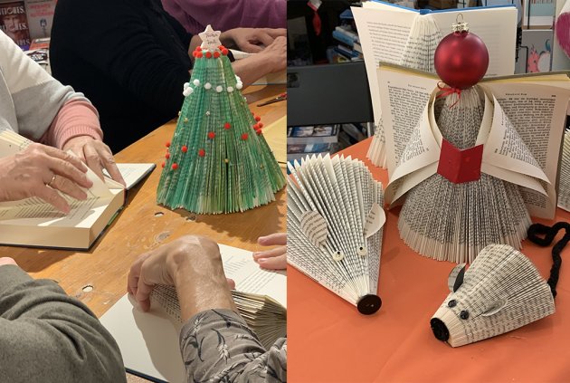 Auf einem Tisch steht ein Weihnachtsbaum, ein Engel und zwei Mäuse aus alten Buchseiten. Hände falten Papier. 