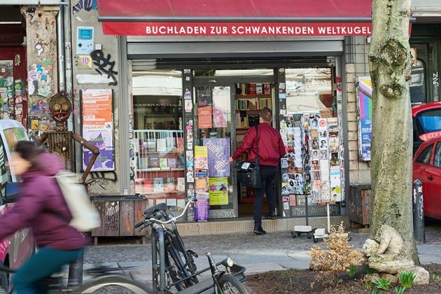 Außenansicht: Eine Person in roter Jacke geht durch die Tür des Buchladen zur Schwankenden Weltkugel in Berlin 