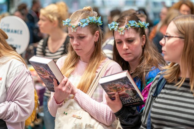 Zwei junge Frauen mit blauen Blumenband im Haar lesen die Beschreibung auf der Rückseite von Büchern