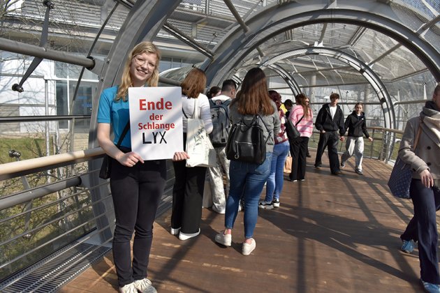 Eine Frau steht im Tunnel-Übergang zwischen den Messehallen und hält ein Schild mit Aufschrift "Ende der Schlange LYX"