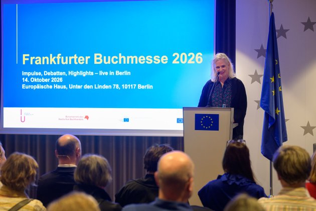Rednerin am Pult vor einer Leinwand, auf der "Frankfurter Buchmesse 2026" steht
