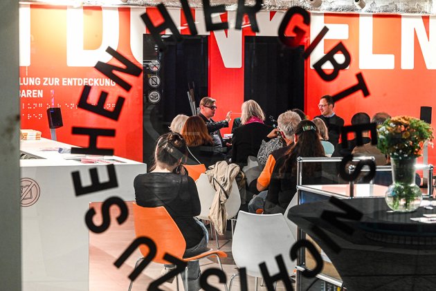 Diskussionsgruppe hinter einer Scheibe mit der Aufschrift "hier gibt es nichts zu sehen"