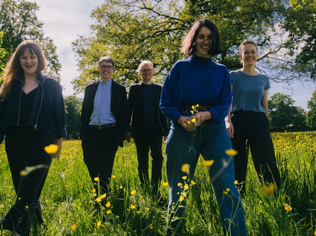 5 PErsonen gehen lachen durch eine Wise mit gelben Blumen