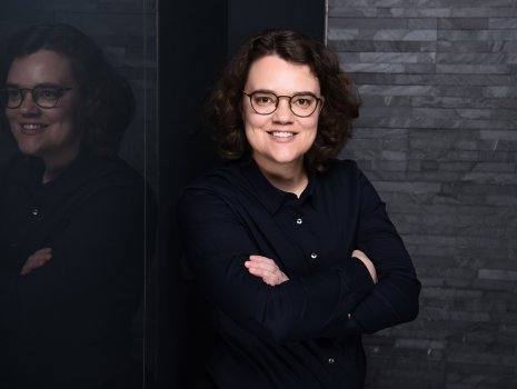 Désirée Kelichhaus in dunkler Bluse mit Brille vor dunklem Studiohintergrund