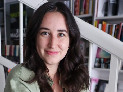 Lilly Ludwig sitzt lächelnd auf einer Treppe vor einem Bücherregal 