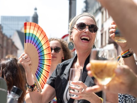 Eine Frau fächert sich mit einem Regenbogen-Fächer Luft zu.