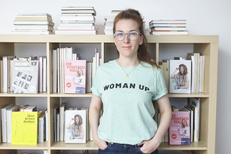 Anne Friebel im T-Shirt vor einem Bücherregal mit den Verlagstiteln