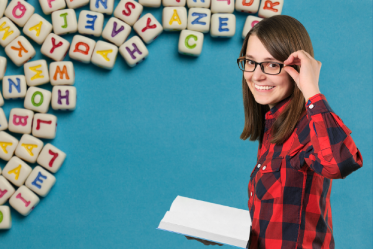 Junge Frau mit aufgeschlagenem Buch und Brille vor vielen bunten Holzbuchstaben