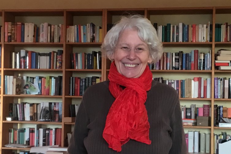 Mechthild Goetze-Hillebrand mit rotem Schal vor einem großen Bücherregal