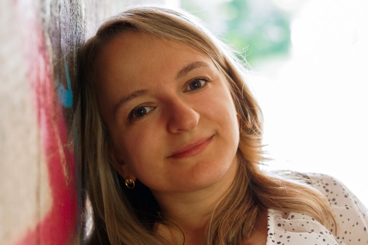 Porträtfoto von Alexandra Koch mit offenem Haar - der Kopf ist an eine Wand mit Graffiti gelehnt