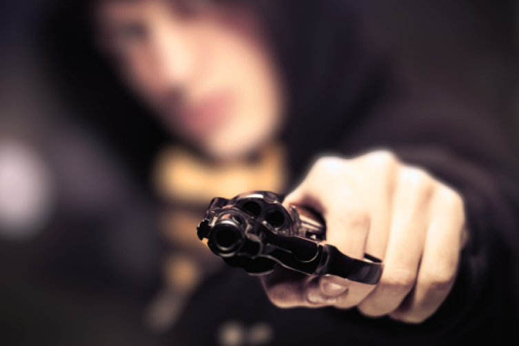 Ein Mann mit Kapuze zielt mit einem Revolver