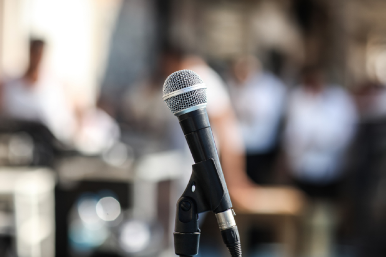 Ein Mikrofon im Vordergrund, unscharf dahinter Menschen 